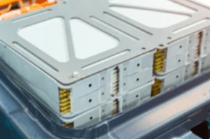 Close-up of a metallic, rectangular battery pack with visible wiring on the edges. The structure shows multiple stacked layers with a grid-like pattern, featuring a mix of silver and yellow hues.