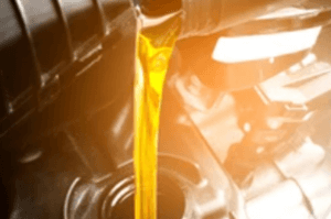 Close-up of golden motor oil being poured into a car engine, with the engine components visible in the background, slightly blurred, under warm lighting.