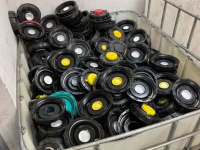 A large container filled with numerous black plastic reels, each with colorful centers in red, yellow, green, or white. The container is situated against a plain wall in an industrial setting.
