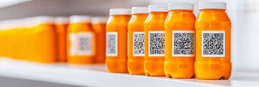 Row of orange bottles with QR codes on a white shelf, with some bottles blurred in the background.