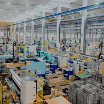 Large industrial factory interior with automated machinery and equipment. The space is organized with conveyor belts, storage bins, and assembly stations, under bright, evenly distributed ceiling lights.