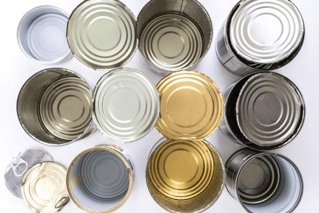 A top view of twelve open, empty metal cans arranged in a grid pattern. The insides are visible, showing different colors such as gold, silver, and gray. The background is a plain light surface.