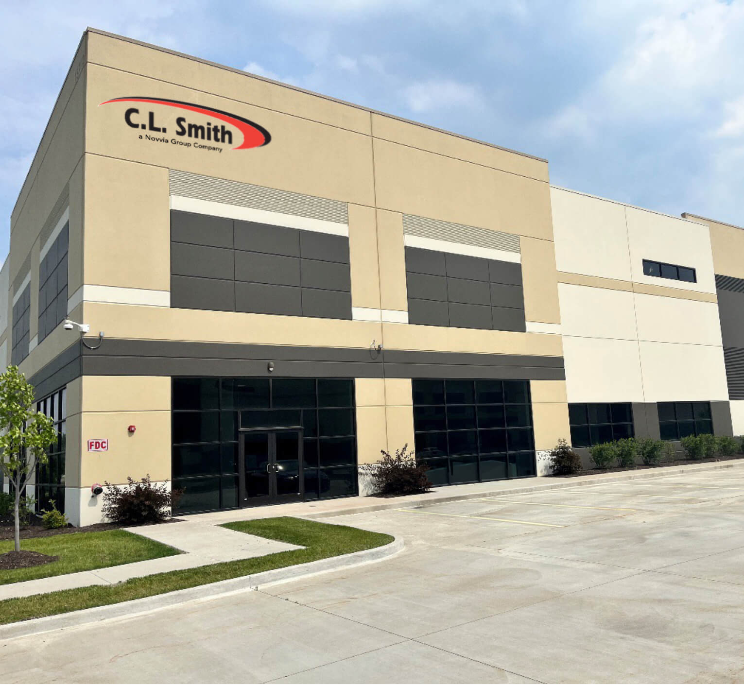 CLS New Building MU A modern beige and gray commercial building with large windows and the "C.L. Smith" logo on the front, situated on a concrete lot under a partly cloudy sky.